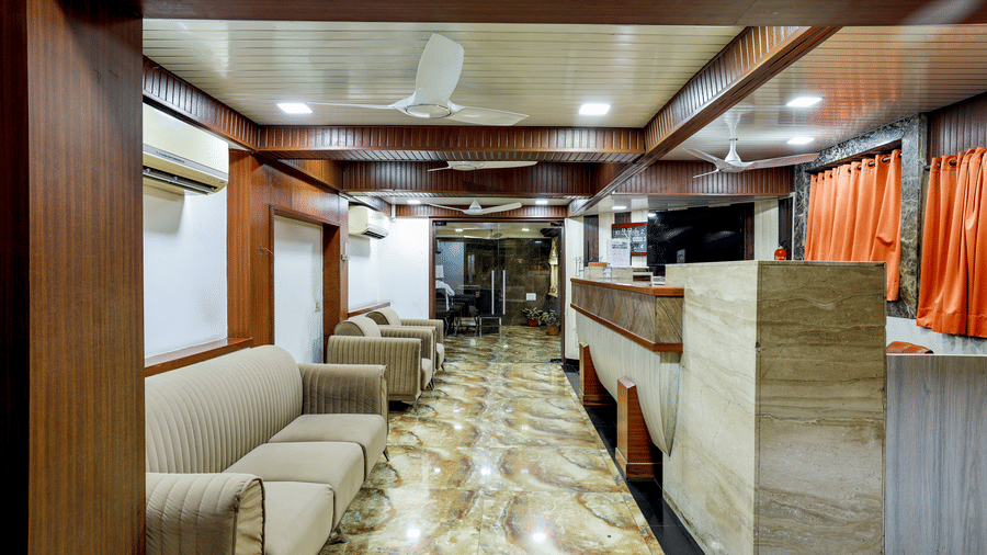 Long view of a lounge area with patterned flooring, sofas lining the walls, and wood-panelled ceilings at Kumar Resort by Turtle.