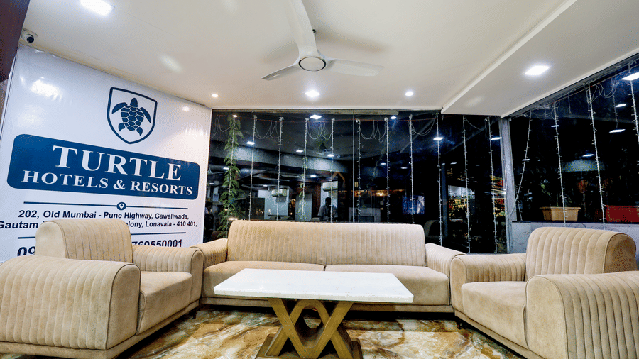 Lobby area with modern sofas, a coffee table, large windows, and a prominent display sign featuring the resort logo and name at Kumar Resort by Turtle.