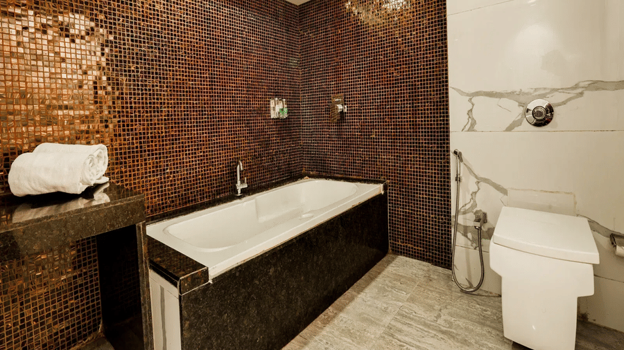 Bathroom at Kumar Resort by Turtle with a soaking tub set against copper mosaic-tile walls, rolled white towel, rain shower and wall-hung toilet.
