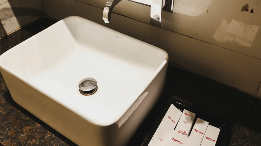 Bathroom vanity at Kumar Resort by Turtle with a white vessel sink, wall-mounted chrome tap and a tray of Kumar-branded toiletry kits.