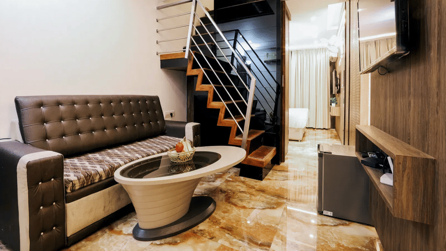 Duplex Suite lower level at Kumar Resort by Turtle with a brown leather sofa, oval coffee table, mounted TV and staircase to upper floor.