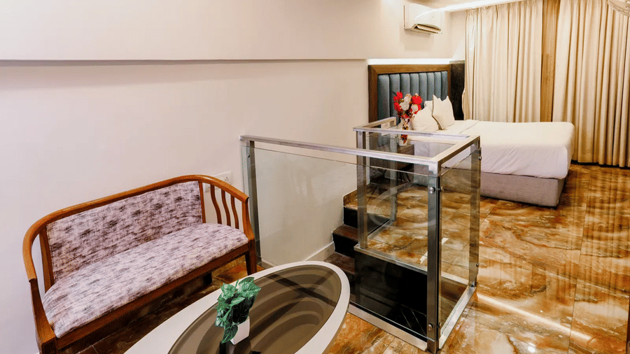 Duplex Suite upper level at Kumar Resort by Turtle with a wooden bench, oval coffee table, glass balustrade and bed visible beyond.