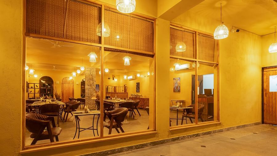 An image of L cave restaurant where walls are made of glass and it has a boho theme featuring several sets of dining tables and chairs - Kurja Jawai