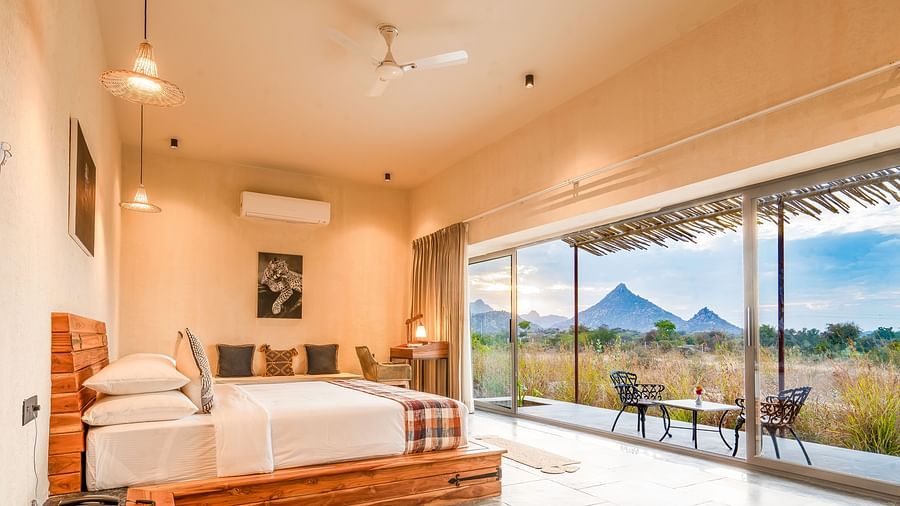 An image of a Stone Cottage bedroom featuring a double size bed, a bedside table, a sofa, a work desk and chair, and a courtyard with seating area at Kurja Jawai