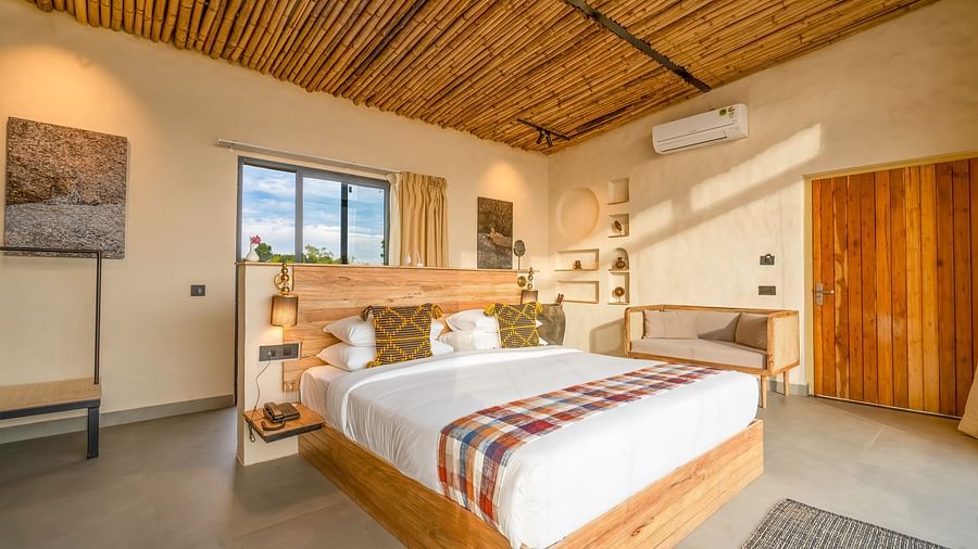 An image of a bedroom featuring a double size, a sofa, ceiling fan, AC, bedside table with lamp, and few decorative elements at Kurja Jawai