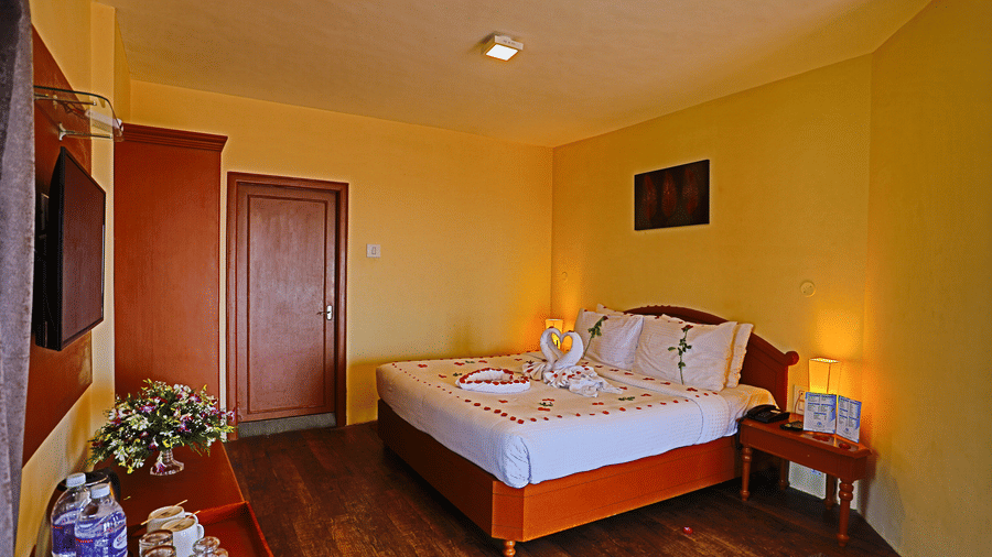 a plush white bed decked with flower petals facing the TV mounted on the wall in a well-lit room and  at La Montana By TGI, Ooty