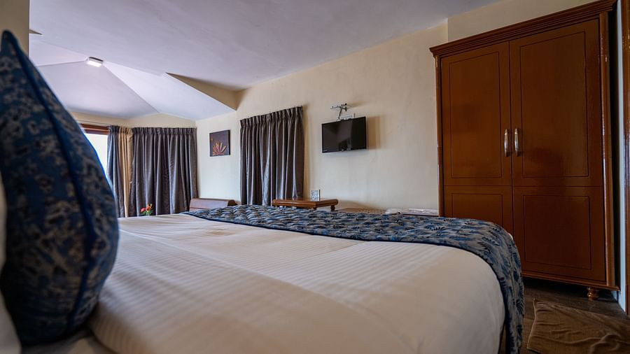 a comfy white bed overlooking a wooden wardrobe at La Montana By TGI, Ooty