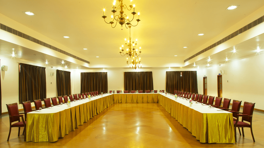 A conference room arranged with a large U-shaped table covered in yellow tablecloths and surrounded by chairs under chandeliers | Le Pondy