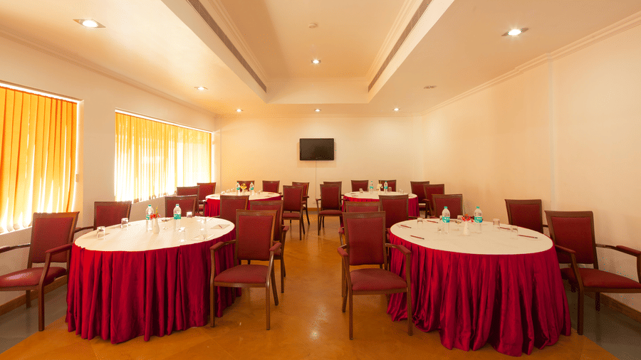 A meeting room arranged with multiple round tables covered in red tablecloths and surrounded by red chairs | Le Pondy