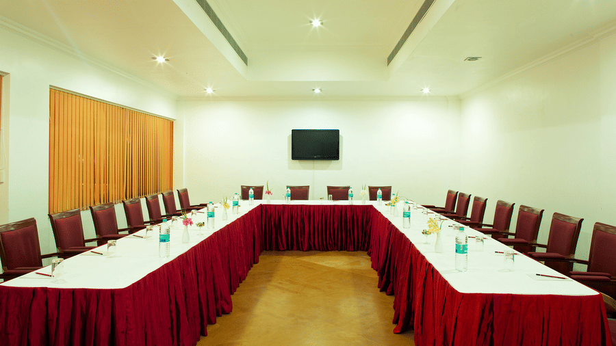 A large meeting room arranged with tables in a U-shape configuration covered with white and red tablecloths, surrounded by chairs | Le Pondy