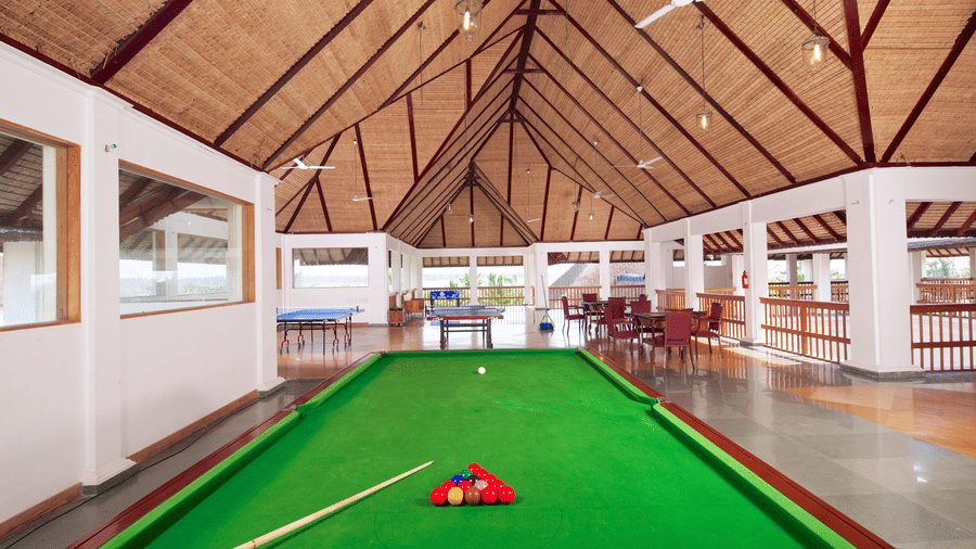 A green pool table with a cue and racked balls in a spacious room featuring a high, vaulted wooden ceiling | Le Pondy