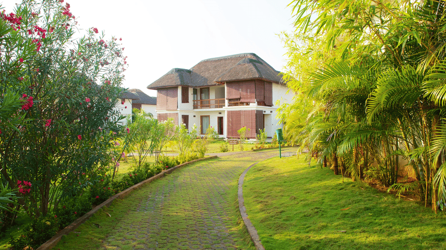 A stone garden path curving through green lawns and trees towards a 2-storey resort villa | Le Pondy