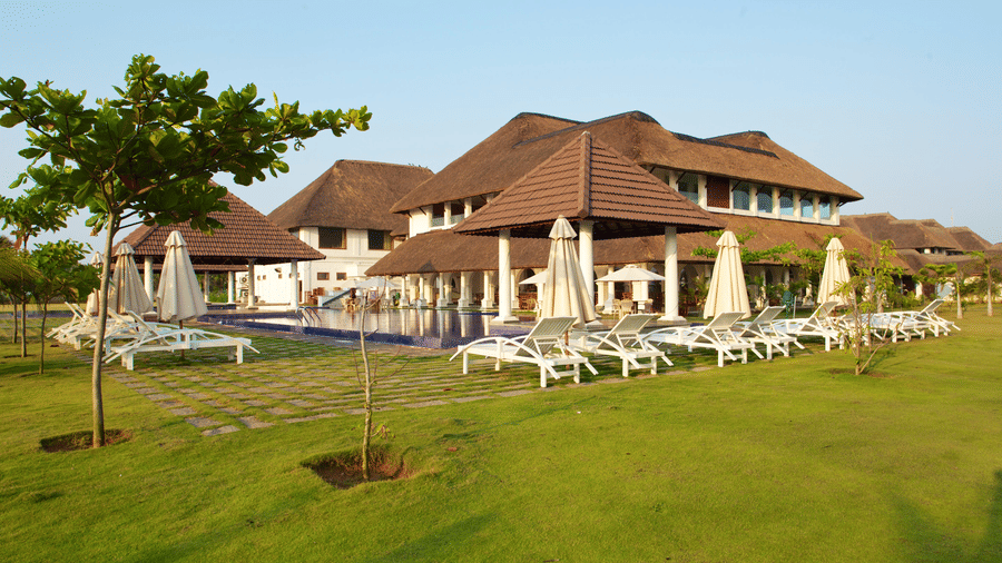 A green lawn with sun loungers and umbrellas situated next to an outdoor swimming pool and resort buildings | Le Pondy