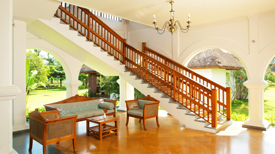 A seating area in a lobby featuring a wooden sofa and armchairs next to a prominent wooden staircase | Le Pondy