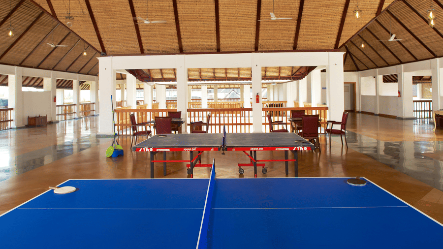 A spacious indoor games hall with a high wooden ceiling featuring 2 blue table tennis tables | Le Pondy