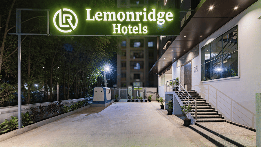Night view of the entrance at Lemonridge Hotels, IDPL Balanagar, featuring the lit signboard and a wide, well-paved approach.