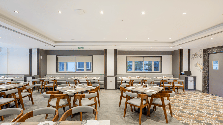 Modern restaurant dining setup with wooden chairs and white tabletops at Lemonridge Hotels, IDPL Balanagar.