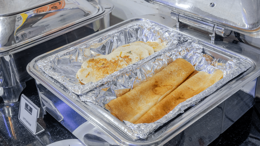 A metal catering tray holds food on foil, with a metal lid open at Lemonridge by Monday Hotels - Kukatpally.
