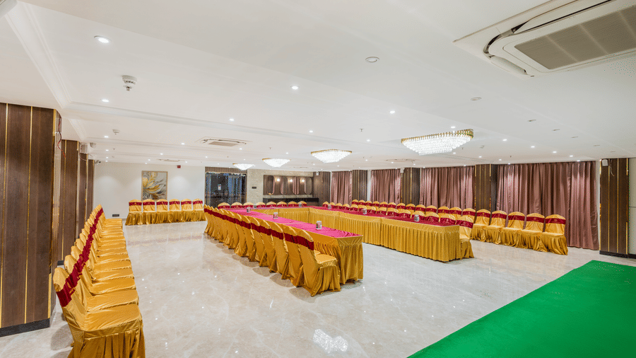 A banquet hall at Lemonridge by Monday Hotels - KPHB featuring long tables, covered chairs, and a ceiling air conditioner unit.