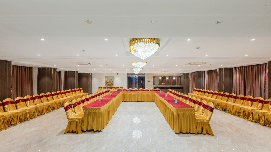 A banquet hall at Lemonridge by Monday Hotels - KPHB featuring long tables, chairs, and a ceiling air conditioner unit.