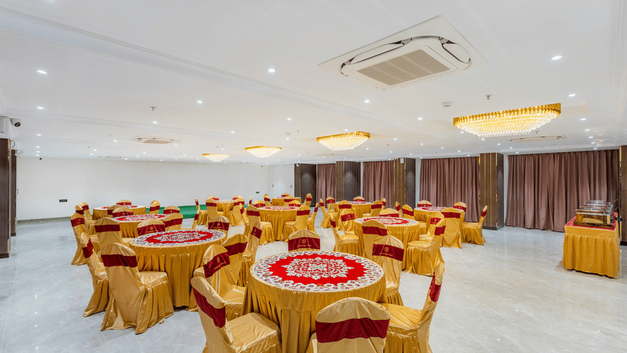 A banquet hall at Lemonridge by Monday Hotels - KPHB featuring round dining tables, covered chairs, and a ceiling air conditioner.