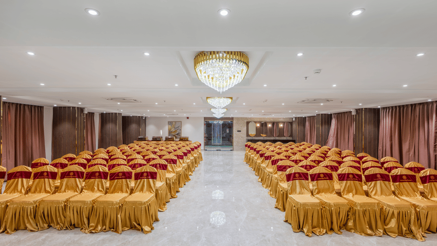 Banquet hall at Lemonridge by Monday Hotels - KPHB featuring hanging crystal chandeliers, rows of chairs, and a small stage.
