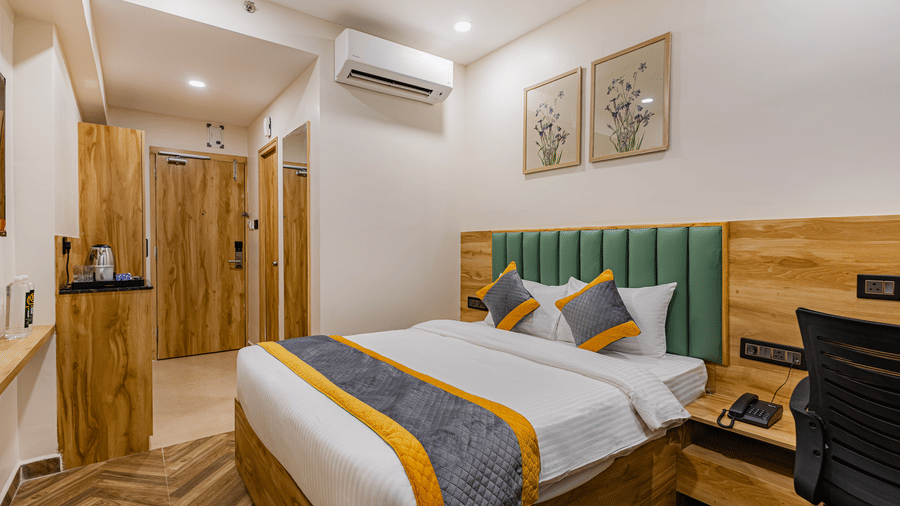 A bedroom at Lemonridge by Monday Hotels - KPHB featuring a large bed, green headboard, framed floral art, an entryway corridor, and an office desk area.