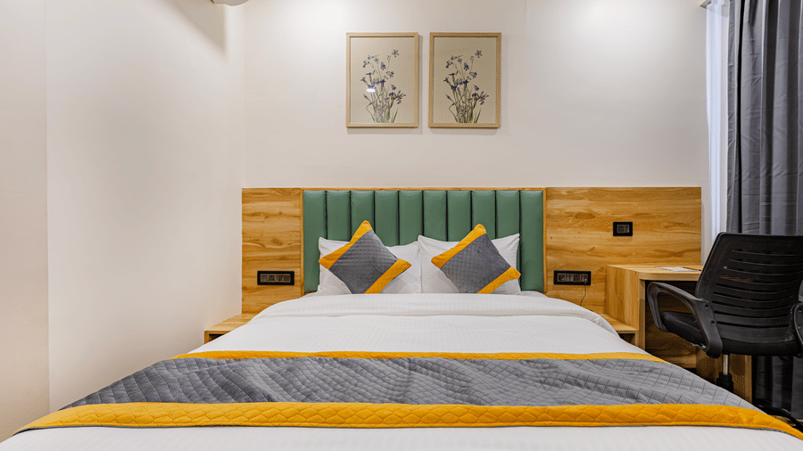 A bedroom at Lemonridge by Monday Hotels - KPHB featuring a large bed, green tufted headboard, framed artwork, a work desk, and grey window drapes.
