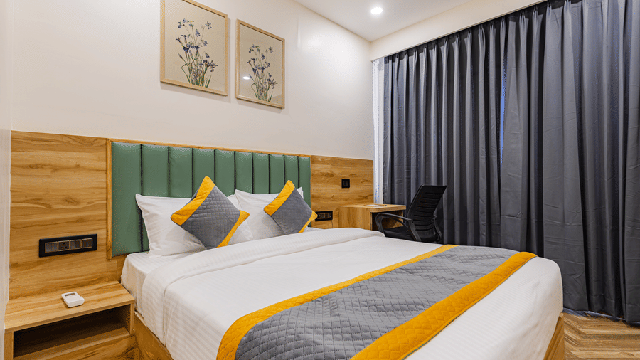 A bedroom at Lemonridge by Monday Hotels - KPHB featuring a large bed, green headboard, framed twin pictures, grey window curtains, and a side study table.