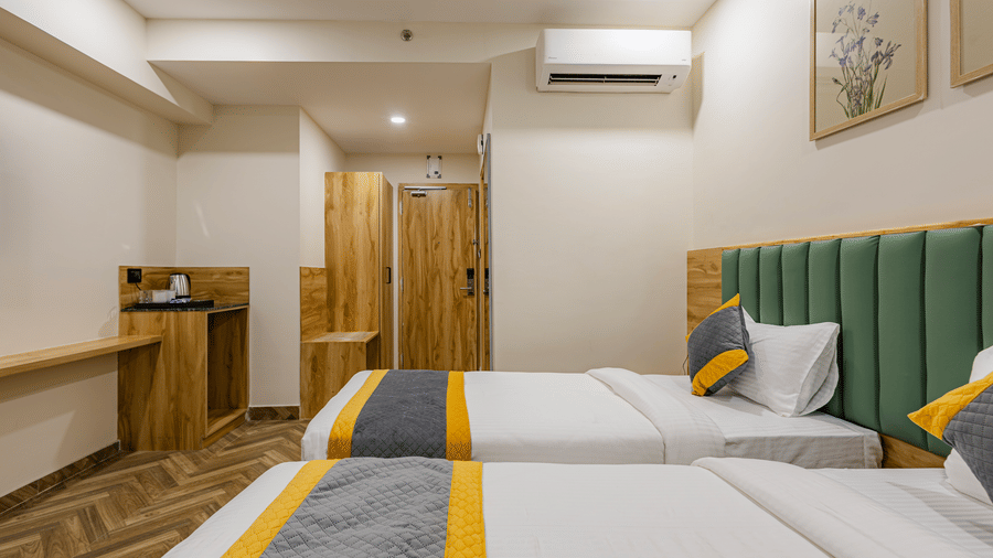 A bedroom at Lemonridge by Monday Hotels - KPHB featuring twin bed, green headboards, wardrobe counter, tea kettle, and AC unit.