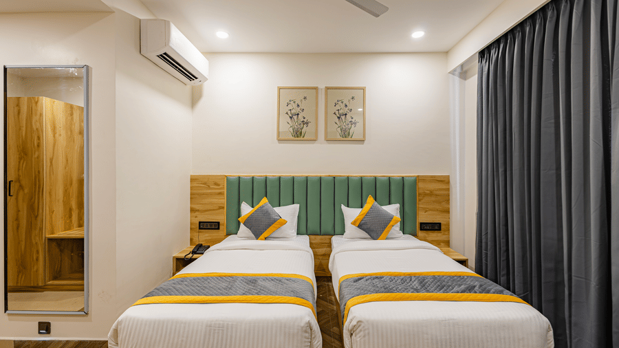 A bedroom at Lemonridge by Monday Hotels - KPHB featuring twin bed, green headboards, dressing mirror, split AC, and window drapes.