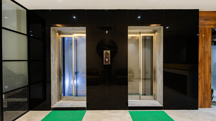 An elevator lobby at Lemonridge by Monday Hotels - KPHB featuring two steel lift doors set against a black accent wall with green floor mats.