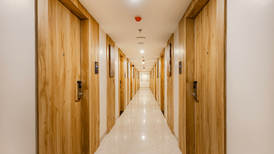 Hallway at Lemonridge by Monday Hotels - KPHB featuring polished cream floor tiles, warm overhead lighting, and matching wooden guest room doors on both sides.