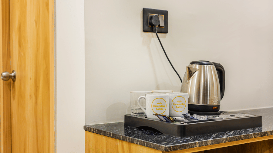 A view of amenities at Lemonridge by Monday Hotels - KPHB featuring an electric kettle, mugs, and sachets on a tray.