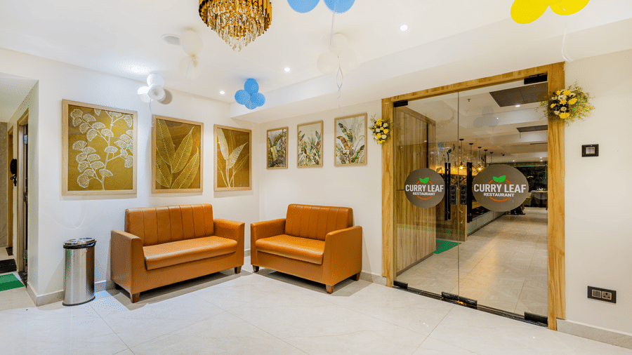 A hallway at Lemonridge by Monday Hotels - KPHB featuring 2 tan sofas, balloon decorations, framed artworks on the wall, and the entrance of Curry Leaf restaurant.