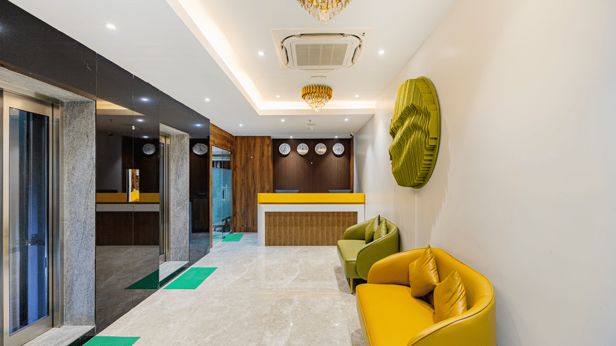 A hotel lobby at Lemonridge by Monday Hotels - KPHB featuring a wood-paneled reception desk, bright yellow and green sofas, and elevators.