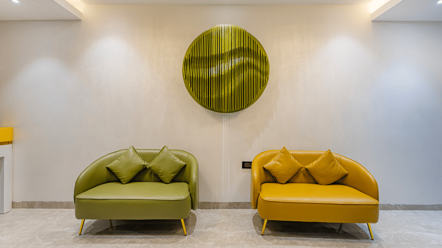A lobby seating area at Lemonridge by Monday Hotels - KPHB featuring an olive green armchair, a yellow sofa, and a round wall ornament.