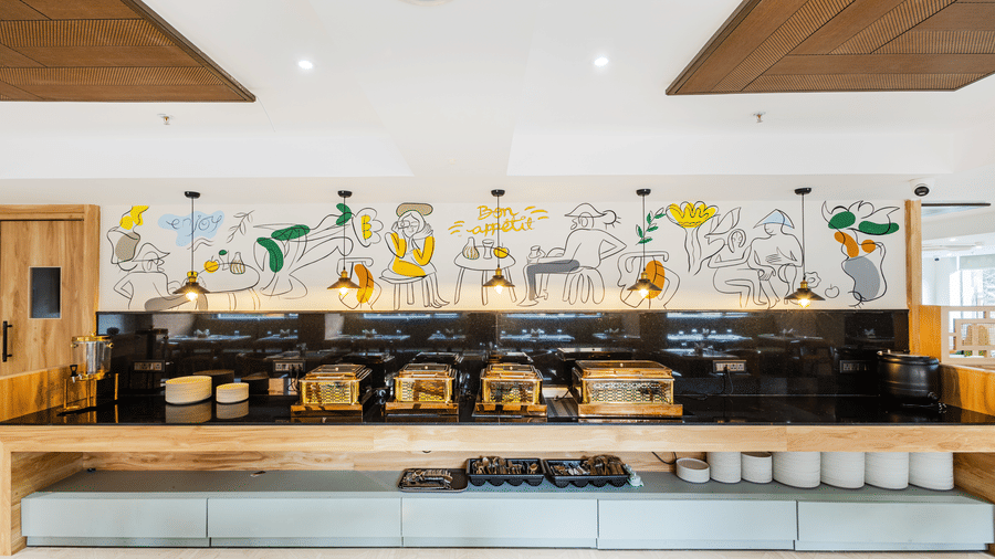 Curry Leaf restaurant at Lemonridge by Monday Hotels - KPHB featuring a long buffet counter, stacked crockery, and line art wall illustrations.