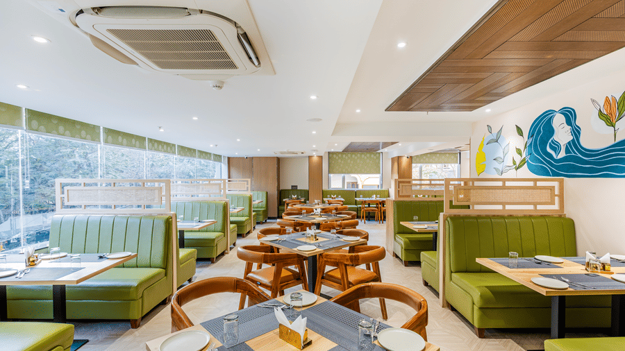 Curry Leaf restaurant at Lemonridge by Monday Hotels - KPHB featuring green booths, set dining tables, wooden chairs, and a ceiling AC unit.