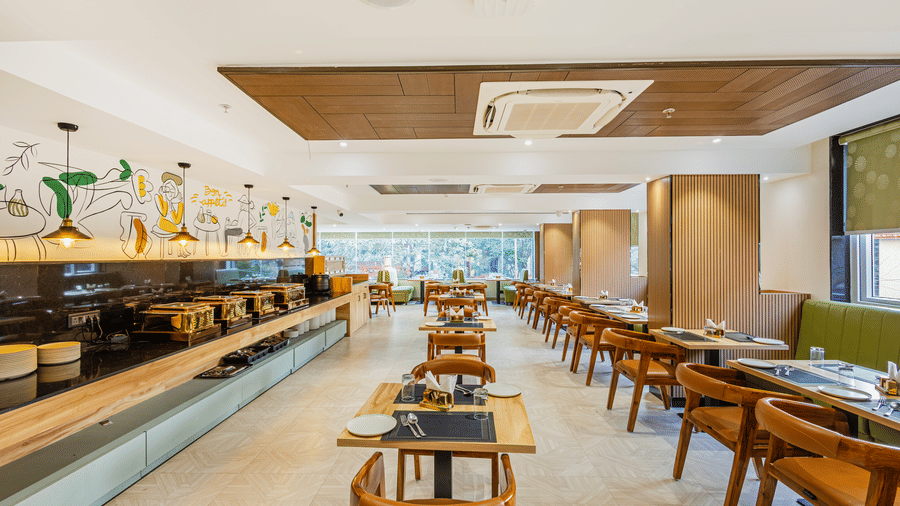 Curry Leaf restaurant at Lemonridge by Monday Hotels - KPHB featuring dining tables, wooden chairs, a buffet counter, and crockery.