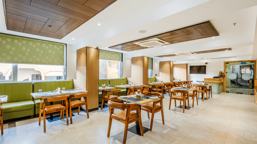 Curry Leaf restaurant at Lemonridge by Monday Hotels - KPHB featuring green booths, wooden tables, bright window blinds, and a ceiling AC unit.