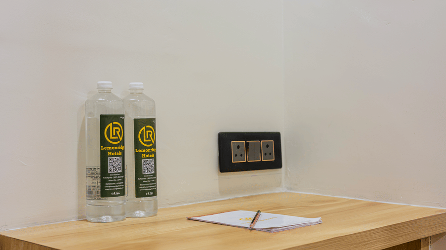A guest writing desk at Lemonridge by Monday Hotels - KPHB featuring a wood table, notepad, water bottles, and switchboard.