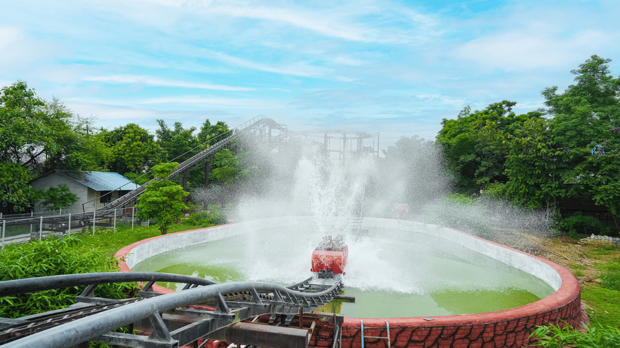 A log flume ride splashes into the water below, sending a dramatic spray into the air beside lush greenery - Lighthouse Waterpark & Resort, Nagpur