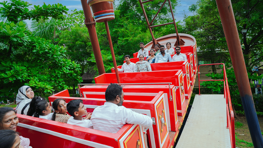 Visitors seated in a bright red open carriage ride moving through a lush, tree-lined area - Lighthouse Waterpark & Resort, Nagpur