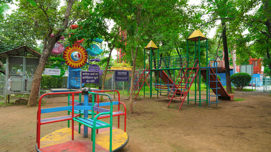 A small roundabout carousel painted in cheerful colours, placed on sandy ground beneath leafy trees - Lighthouse Waterpark & Resort, Nagpur