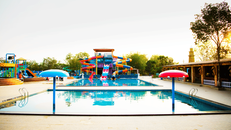A sunny, outdoor swimming pool at a Lighthouse Waterpark & Resort, Nagpur with slides and colourful features.