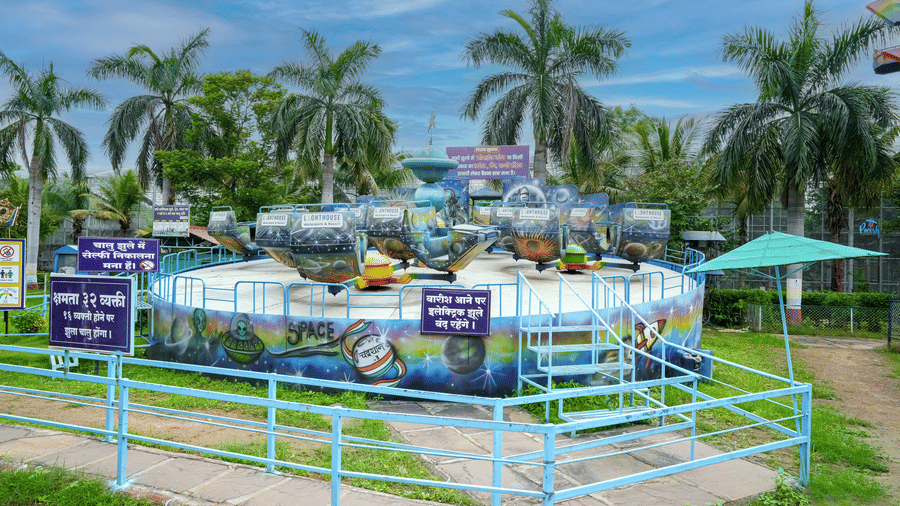 A compact water play area with shallow pools and slides, enclosed by fencing and lined with palm trees.