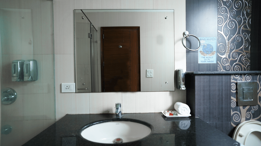 Bathroom with a granite vanity, undermount sink, a large mirror, two wall soap dispensers, a towel ring, and a rolled towel.