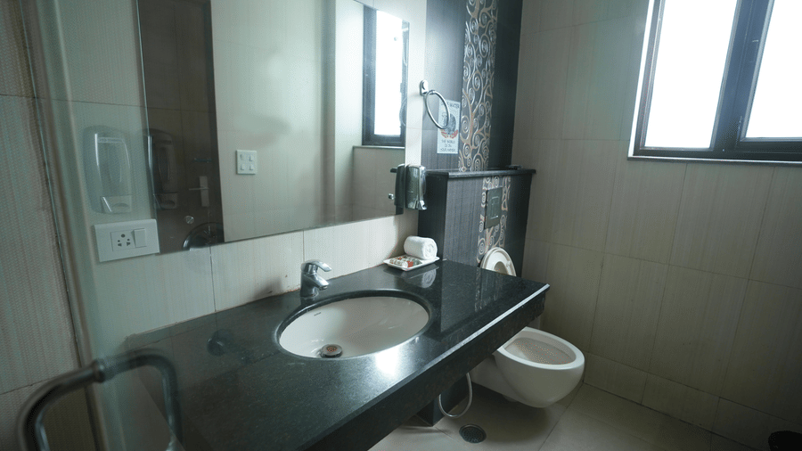 Bathroom with a granite vanity, sink, mirror, a wall soap dispenser, a rolled towel, a wall-hung toilet, and a frosted window.