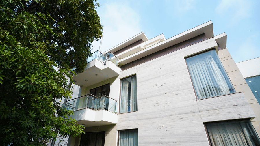 Exterior with a stone-clad low-rise facade, balconies with glass railings, curtained corner windows, and a tree under blue sky.